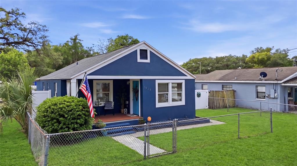 A blue house with a front porch, American flag, and chain-link fence in the yard — 1613 E CHELSEA STREET, TAMPA, FL