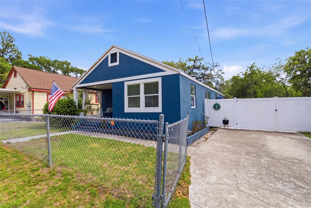 A blue house with a front porch, a chain-link fence, and a concrete driveway — 1613 E CHELSEA STREET, TAMPA, FL