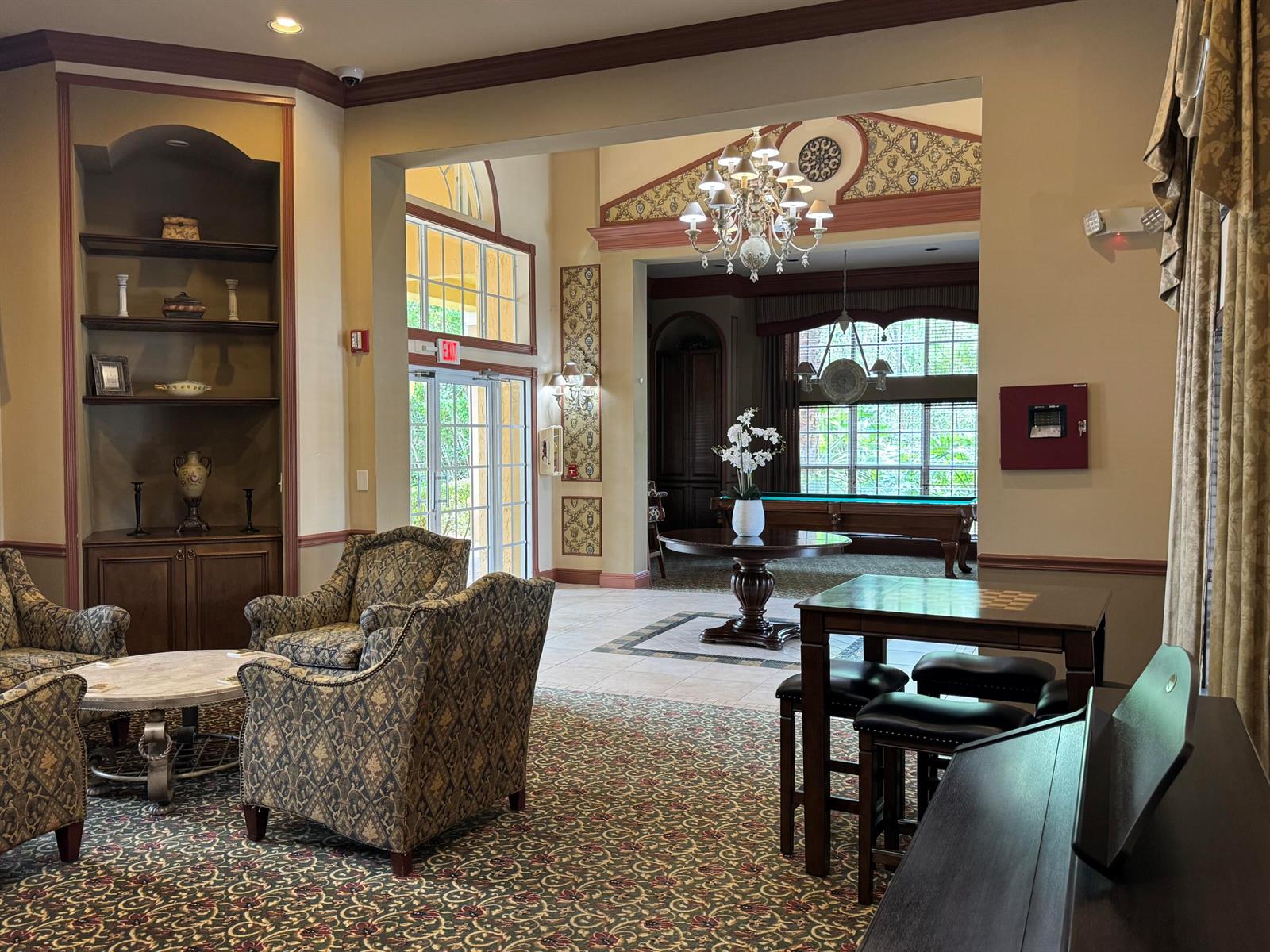 A spacious clubhouse lounge features patterned carpeting, armchairs, a pool table, and a chandelier — 700 Scotia Drive # 103, Hypoluxo FL 33462, HYPOLUXO, FL