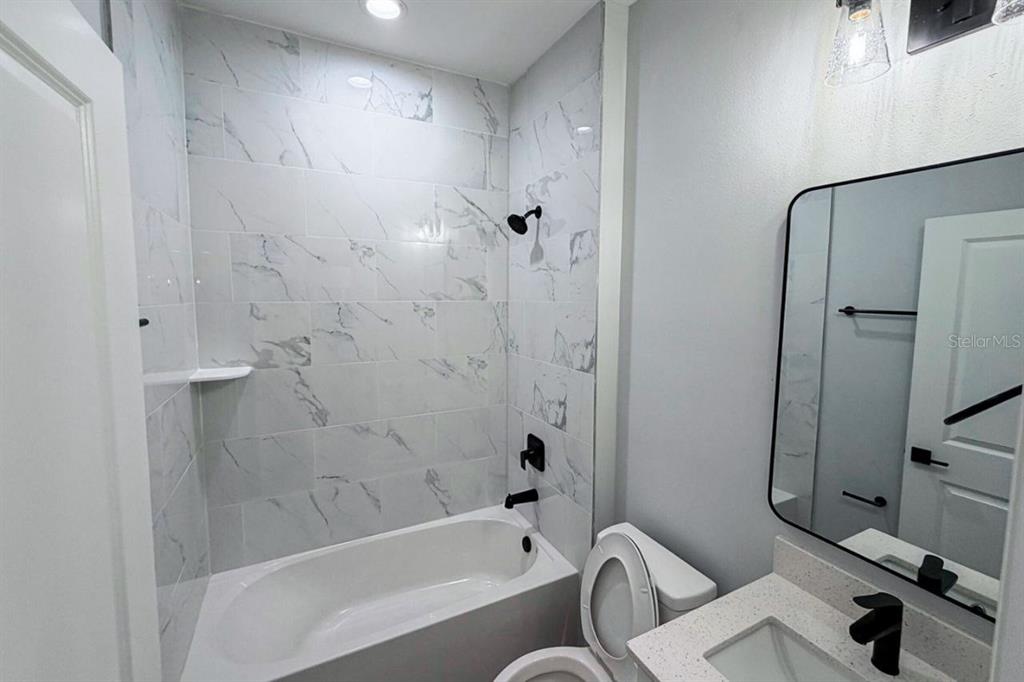 A bathroom features a white marble-tiled tub shower, a vanity with a mirror, and a toilet — 17381 TYLER AVENUE, PORT CHARLOTTE, FL