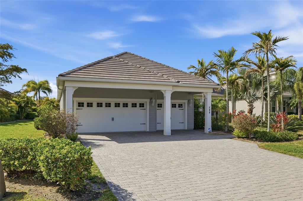 A paved driveway leads to a two-car garage with a tiled hip roof and palm trees — 548 REGATTA WAY, BRADENTON, FL