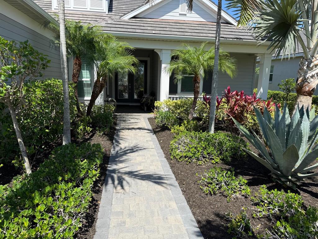 A paved walkway leads to the front entrance of a house with palm trees and landscaping — 548 REGATTA WAY, BRADENTON, FL