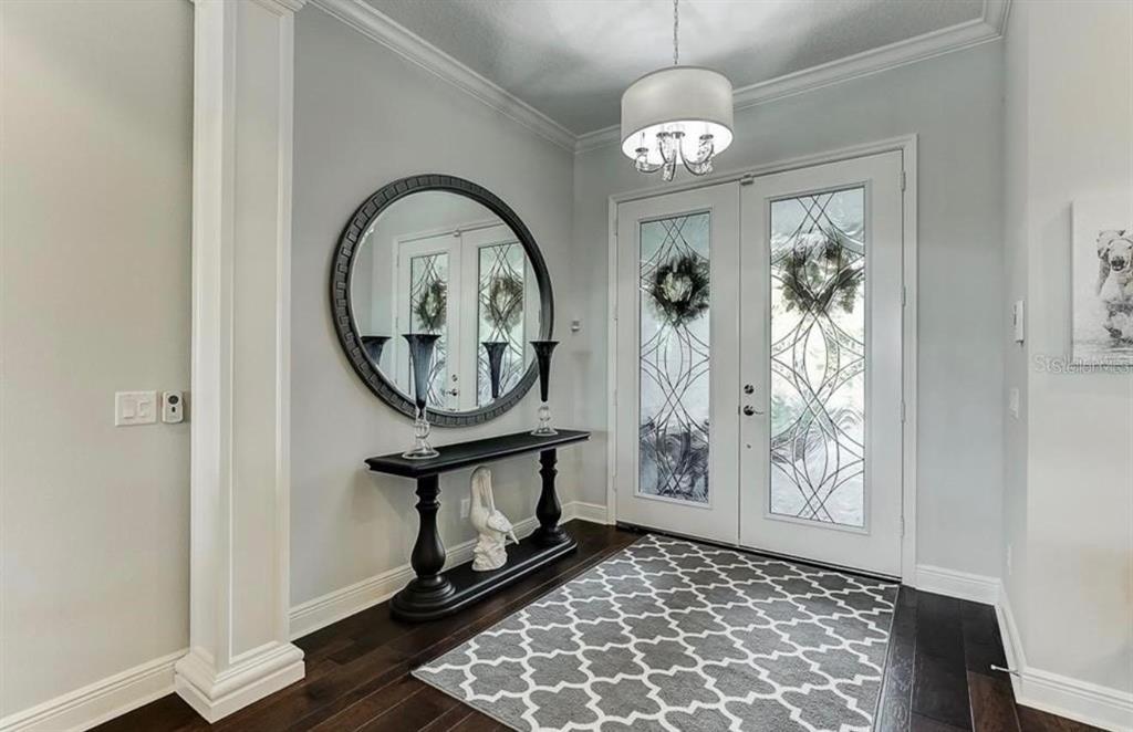 An entryway features a dark wood console table, a round mirror, and a patterned area rug — 548 REGATTA WAY, BRADENTON, FL