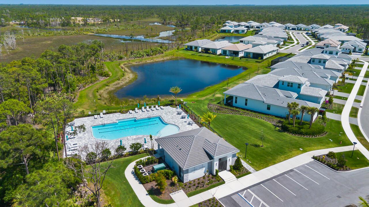 An aerial view shows a community swimming pool, clubhouse, and surrounding residential homes near wetlands — 6980 SE Haven Lane, Stuart FL 34997, STUART, FL