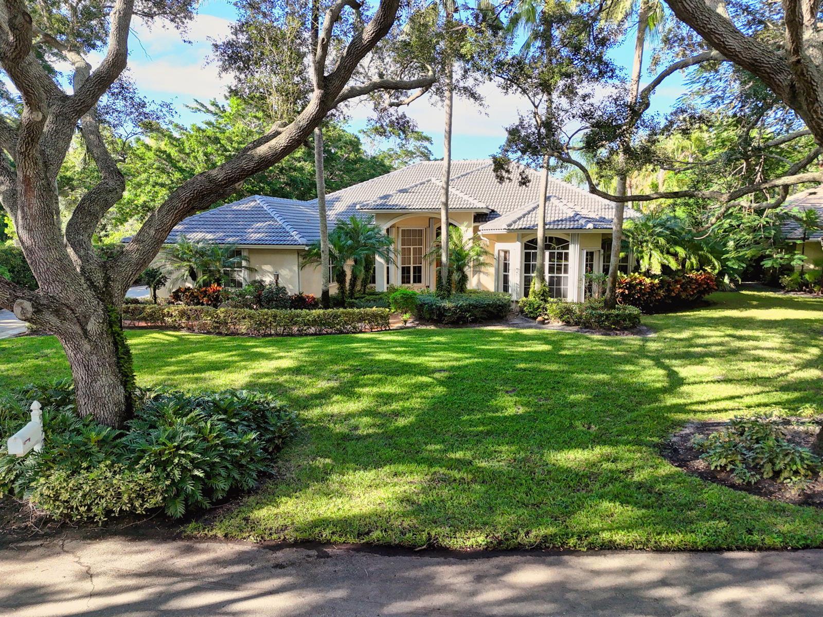 A single-story house with a tiled roof, beige stucco exterior, and lush landscaping — 9923 SE Oak Tree Terrace, Tequesta FL 33469, TEQUESTA, FL