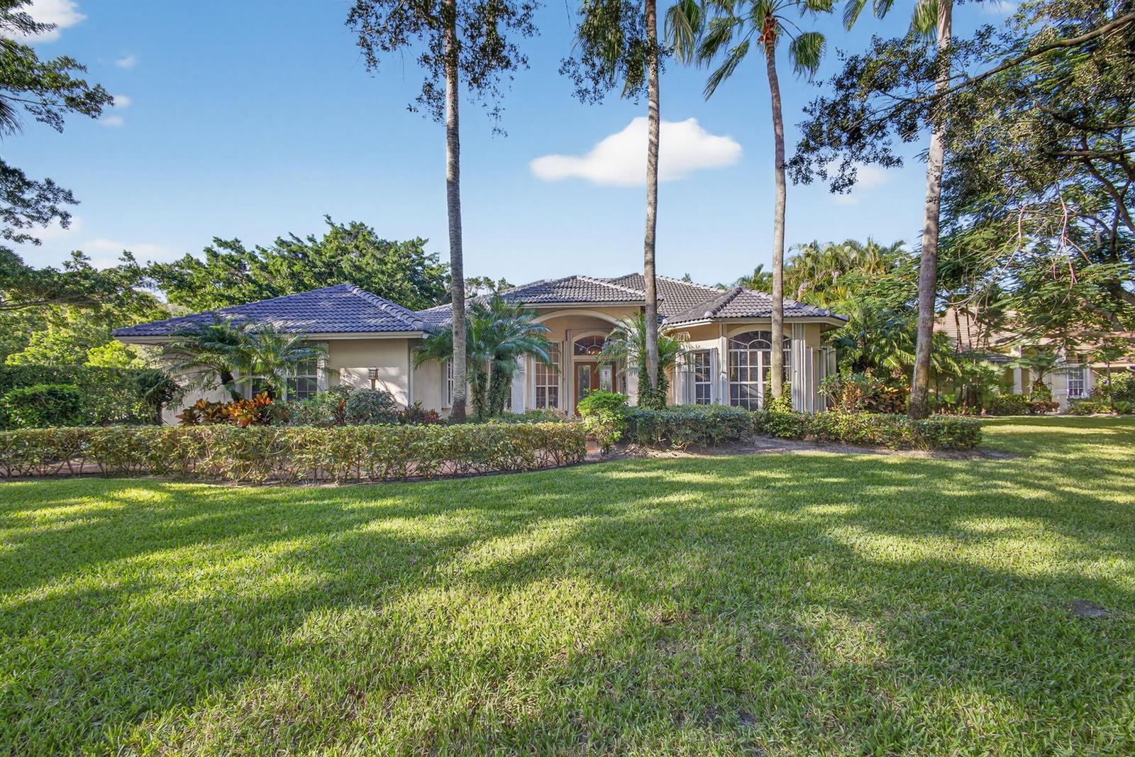A single-story house with a tiled roof and palm trees sits behind a manicured lawn — 9923 SE Oak Tree Terrace, Tequesta FL 33469, TEQUESTA, FL