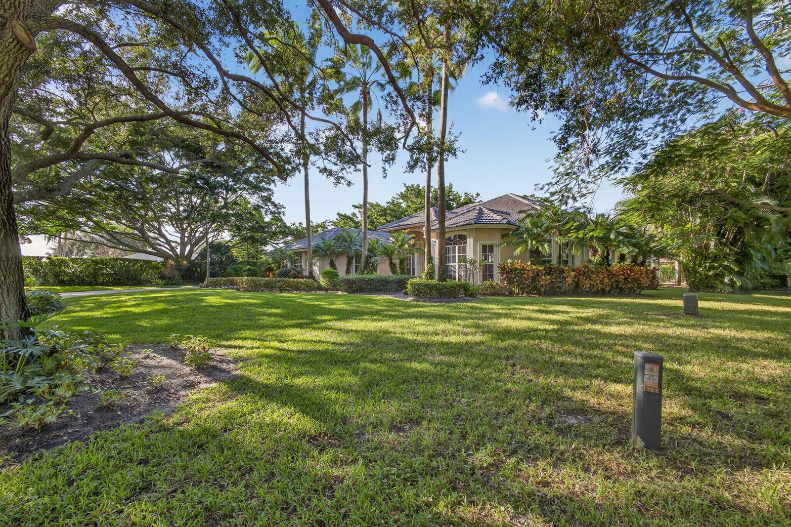 A single-story house with a tiled roof sits behind a large, grassy lawn and trees — 9923 SE Oak Tree Terrace, Tequesta FL 33469, TEQUESTA, FL