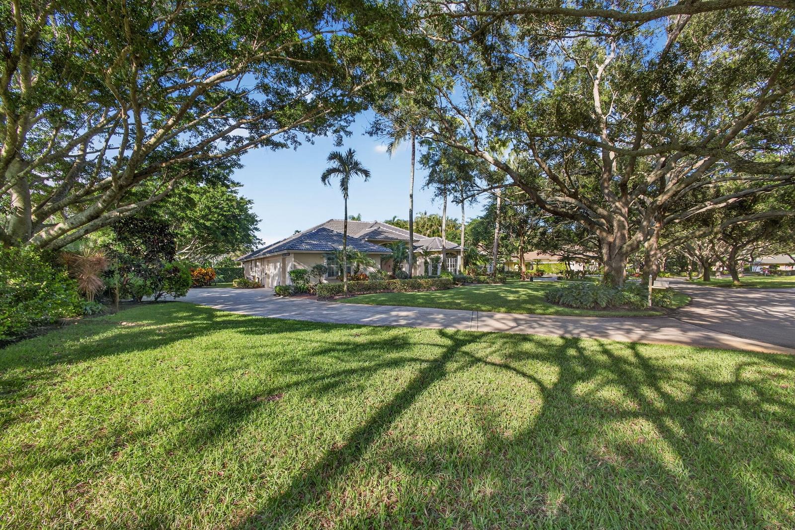 A single-story house with a tile roof sits behind a large lawn and mature trees — 9923 SE Oak Tree Terrace, Tequesta FL 33469, TEQUESTA, FL