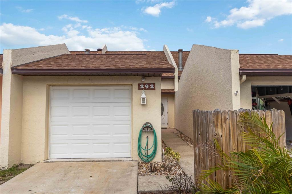 A single-story townhouse exterior features a white garage door, a front entrance, and a hose — 292 CANAVERAL BEACH BOULEVARD, CAPE CANAVERAL, FL
