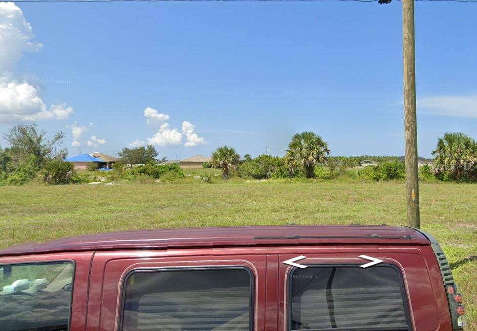 A view of a vacant grassy lot with a utility pole and a vehicle foreground — 4042 NW 37TH AVENUE, CAPE CORAL, FL