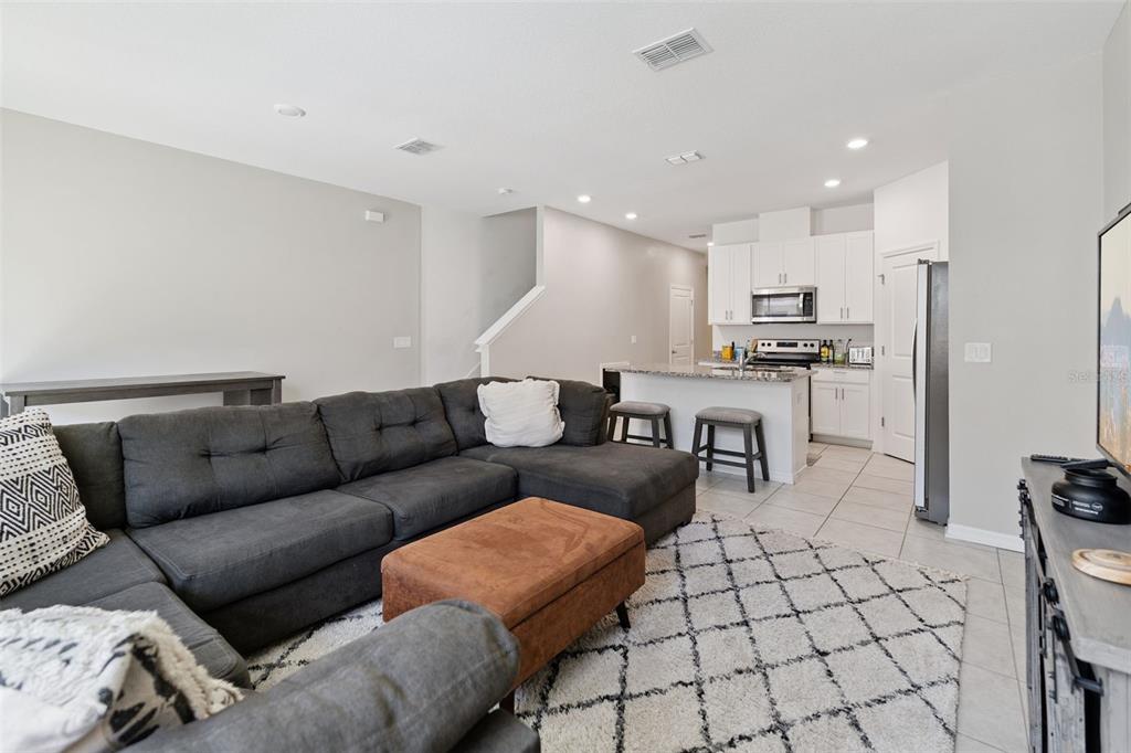 A living room with a gray sectional sofa, brown ottoman, and an open kitchen beyond — 1106 ARBOUR VERDE COURT, TAMPA, FL