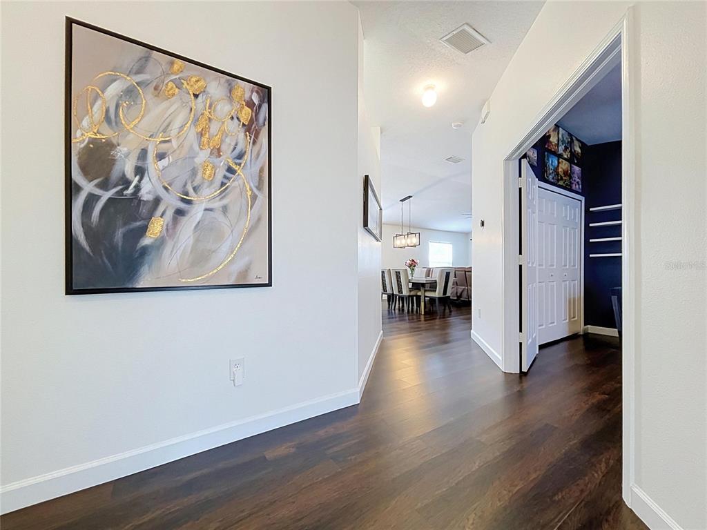 A hallway with dark wood flooring leads to a dining area with a chandelier — 7710 CARRIAGE POINTE DRIVE, GIBSONTON, FL