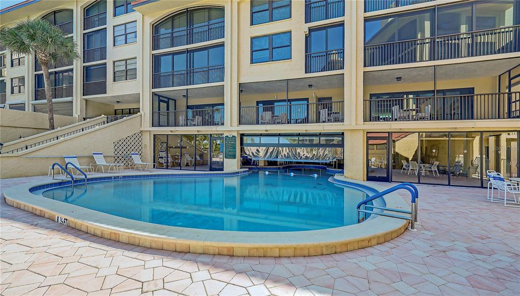 A swimming pool sits on a paved patio in front of a multi-story apartment building — 8710 MIDNIGHT PASS ROAD UNIT 405, SARASOTA, FL