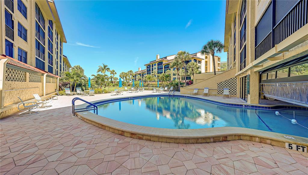 A swimming pool surrounded by a paved deck and multi-story residential buildings under a blue sky — 8710 MIDNIGHT PASS ROAD UNIT 405, SARASOTA, FL