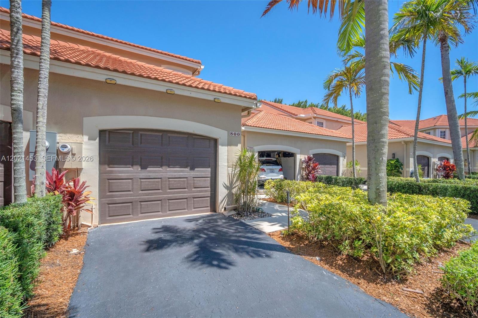 The exterior of a beige residential building features a brown garage door and tiled roof — 800 Sorrento Dr. # 2, Weston FL 33326, WESTON, FL