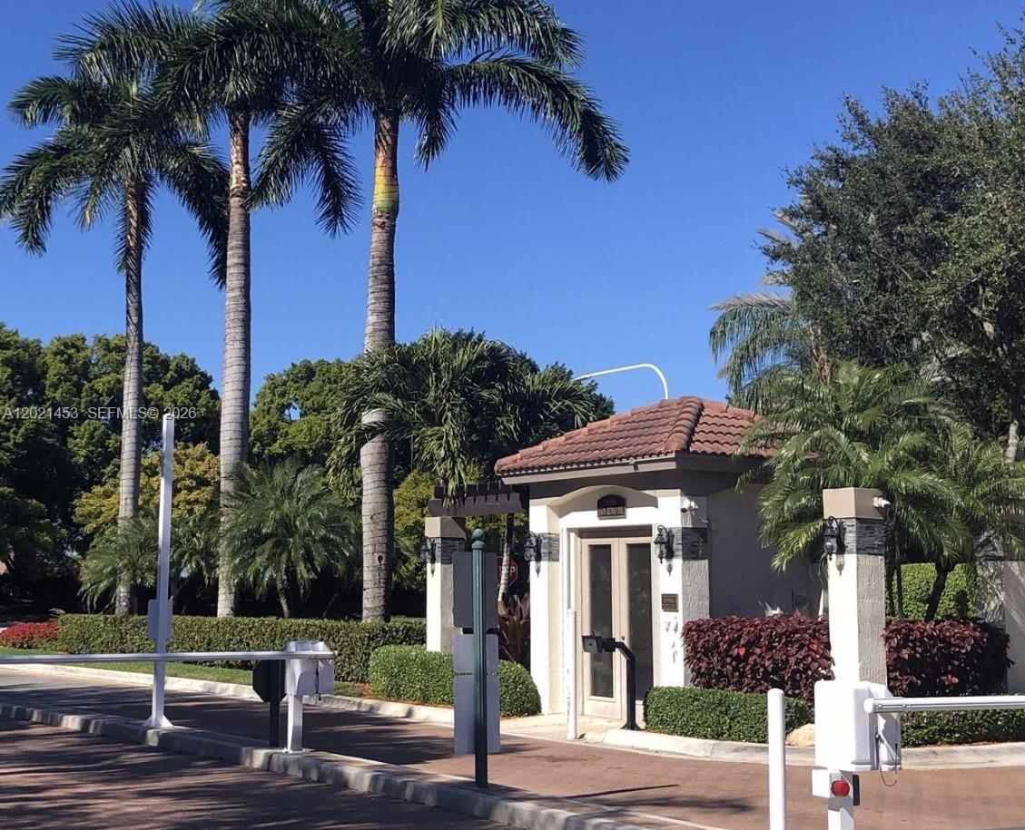 A gated entrance with a guardhouse, palm trees, and a paved driveway under a blue sky — 800 Sorrento Dr. # 2, Weston FL 33326, WESTON, FL