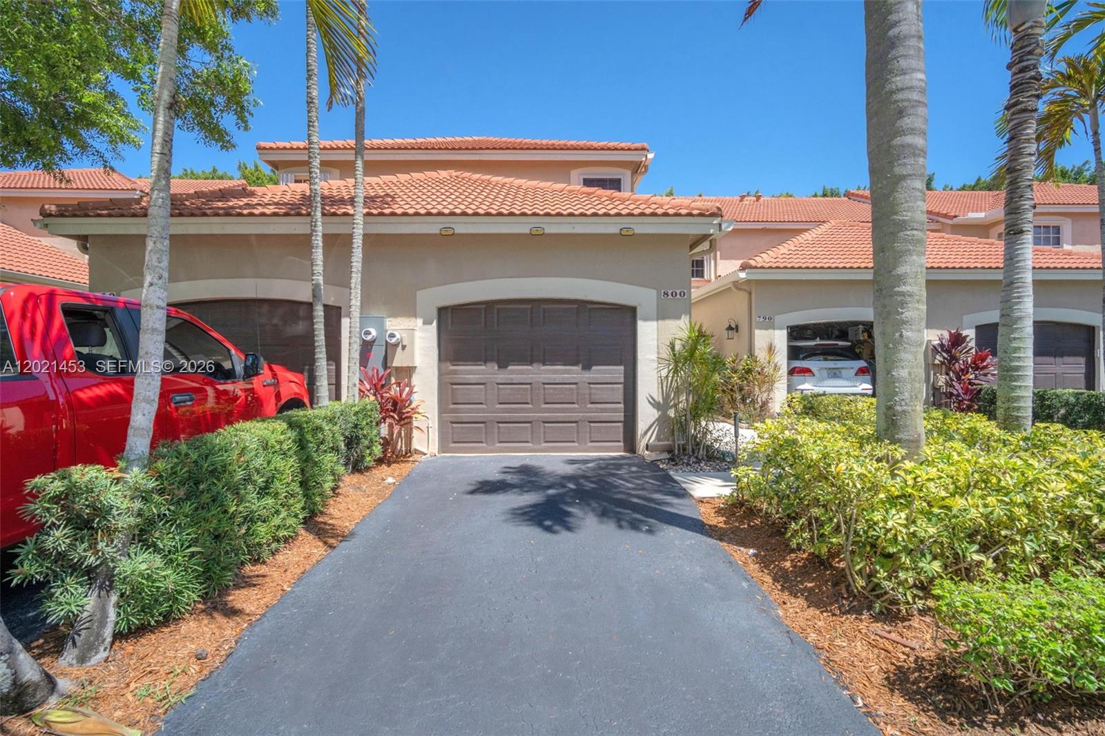 A tan two-story townhouse features a brown garage door and a paved driveway — 800 Sorrento Dr. # 2, Weston FL 33326, WESTON, FL