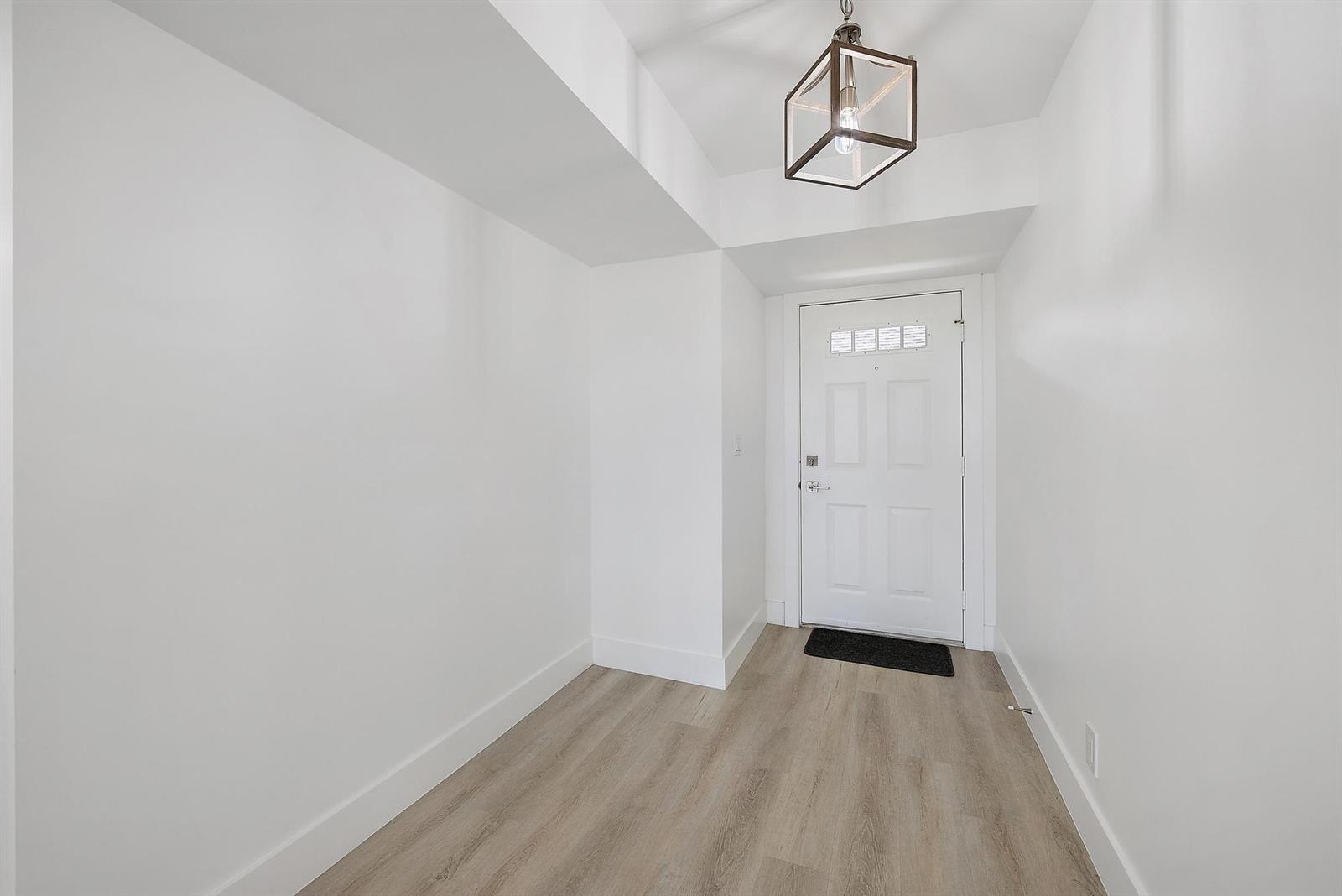 An entryway features white walls, light wood-look flooring, and a modern geometric pendant light — 10459 SE Terrapin Place # 101d, Jupiter FL 33469, JUPITER, FL