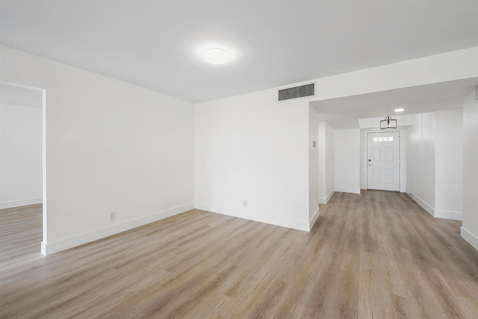 An empty room with white walls, light wood-look flooring, and a white entry door — 10459 SE Terrapin Place # 101d, Jupiter FL 33469, JUPITER, FL