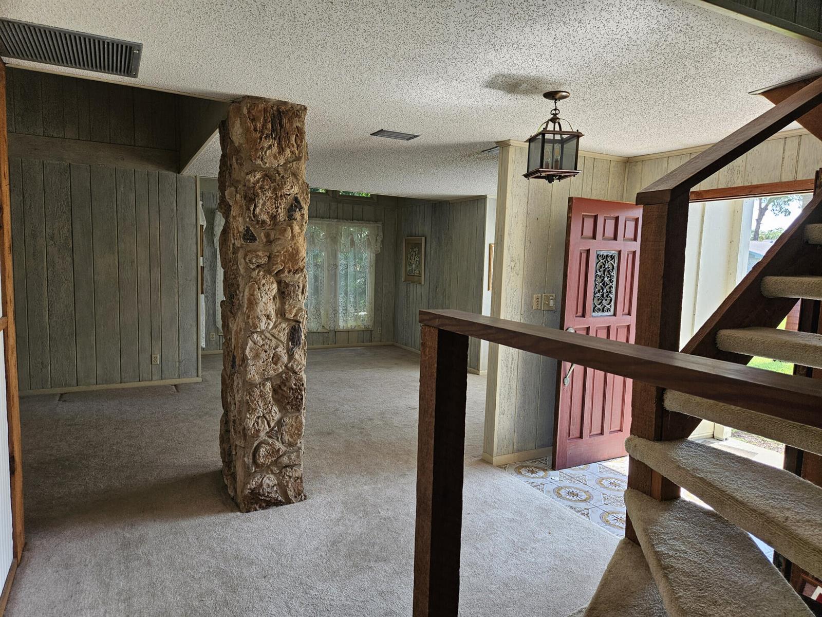 A living room features a stone pillar, wood-paneled walls, carpeted floors, and a wooden staircase — 596 Greenwood Drive, Jupiter FL 33458, JUPITER, FL