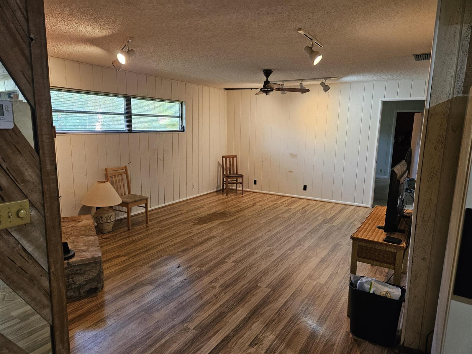 A living room with white vertical paneling, wood-look flooring, a ceiling fan, and track lighting — 596 Greenwood Drive, Jupiter FL 33458, JUPITER, FL