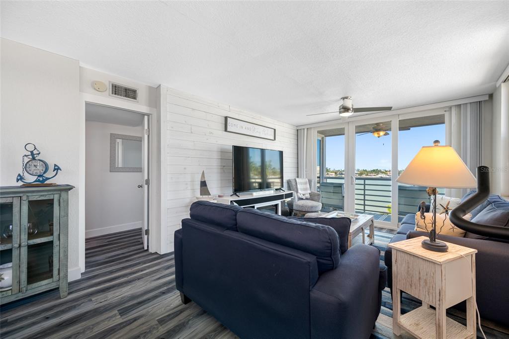 A living room features a blue sofa, white shiplap wall, and a balcony with water views — 5701 BAHIA DEL MAR CIRCLE UNIT 408, ST PETERSBURG, FL