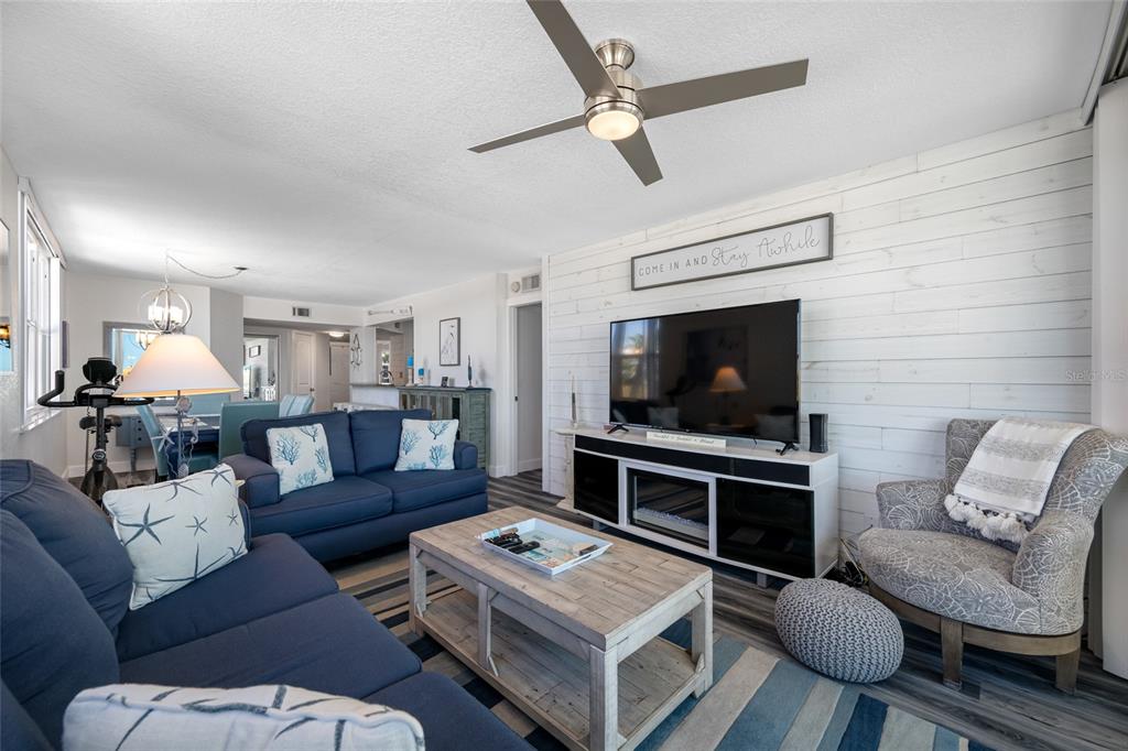 A living room features a blue sofa, a patterned armchair, and a white shiplap wall — 5701 BAHIA DEL MAR CIRCLE UNIT 408, ST PETERSBURG, FL