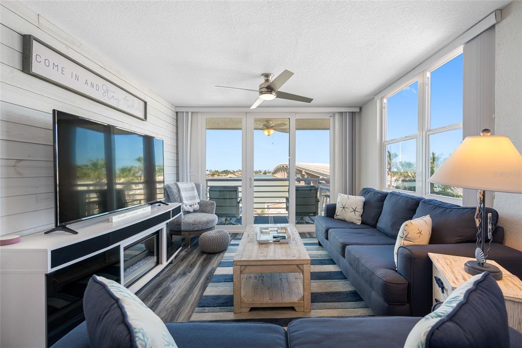 A living room features a blue sofa, a television, and a balcony overlooking a bridge — 5701 BAHIA DEL MAR CIRCLE UNIT 408, ST PETERSBURG, FL