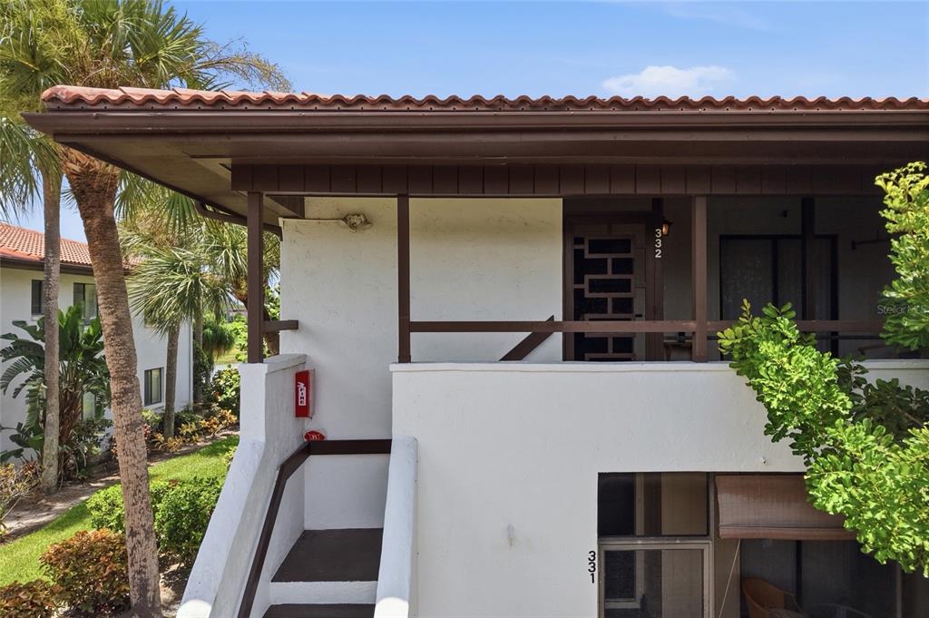 An exterior view of a two-story building with a staircase leading to an upper balcony — 3500 EL CONQUISTADOR PARKWAY UNIT 332, BRADENTON, FL