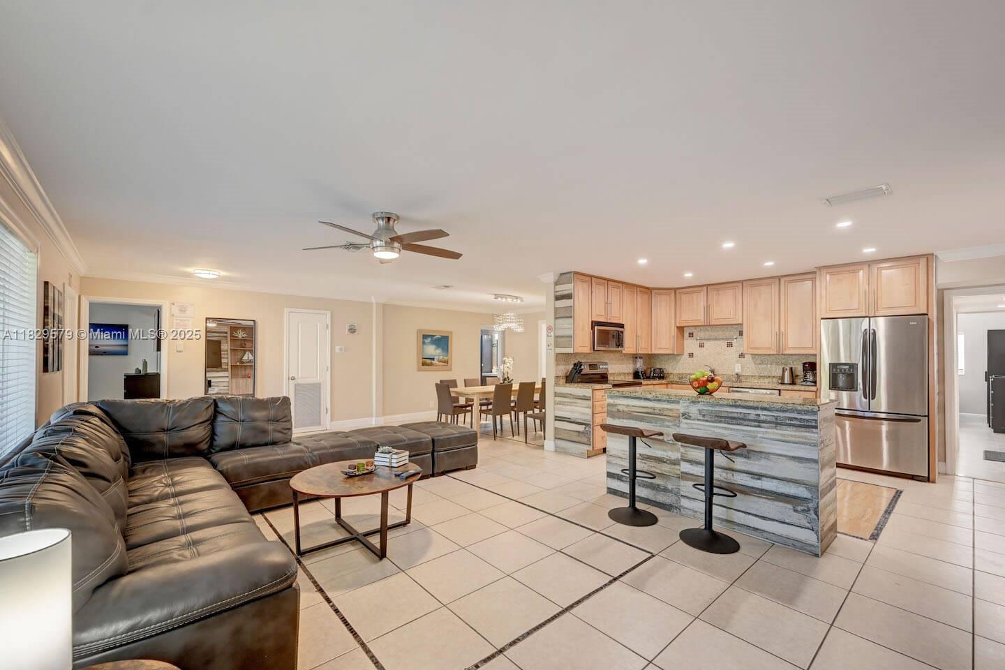 An open-concept living room and kitchen featuring a leather sectional, tile floors, and wood-paneled island — 1228 Johnson St, Hollywood FL 33019, HOLLYWOOD, FL