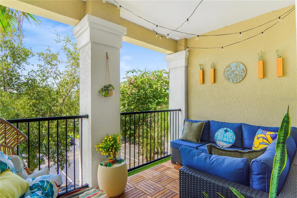 A covered balcony features wicker furniture with blue cushions, wood-look flooring, and string lights — 3605 CONROY ROAD UNIT 535, ORLANDO, FL