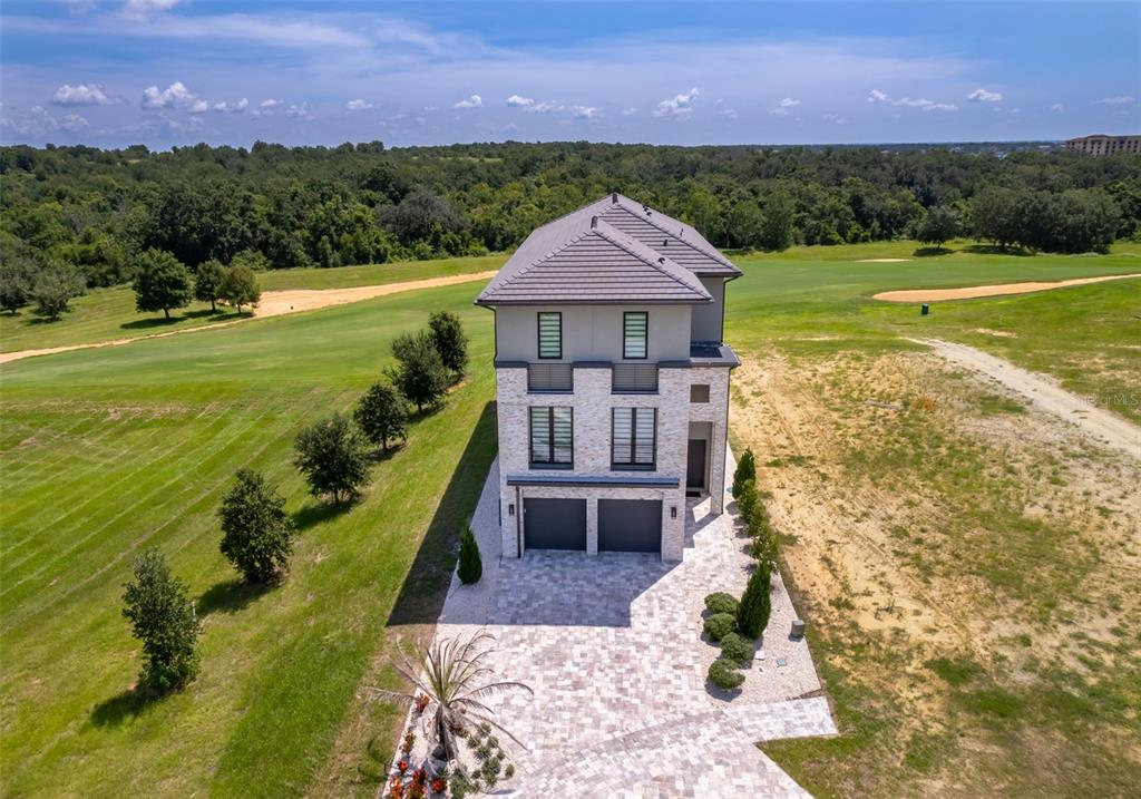 An aerial view of a three-story house with a stone facade and a paved driveway — 16338 RAVENNA COURT, BELLA COLLINA, FL