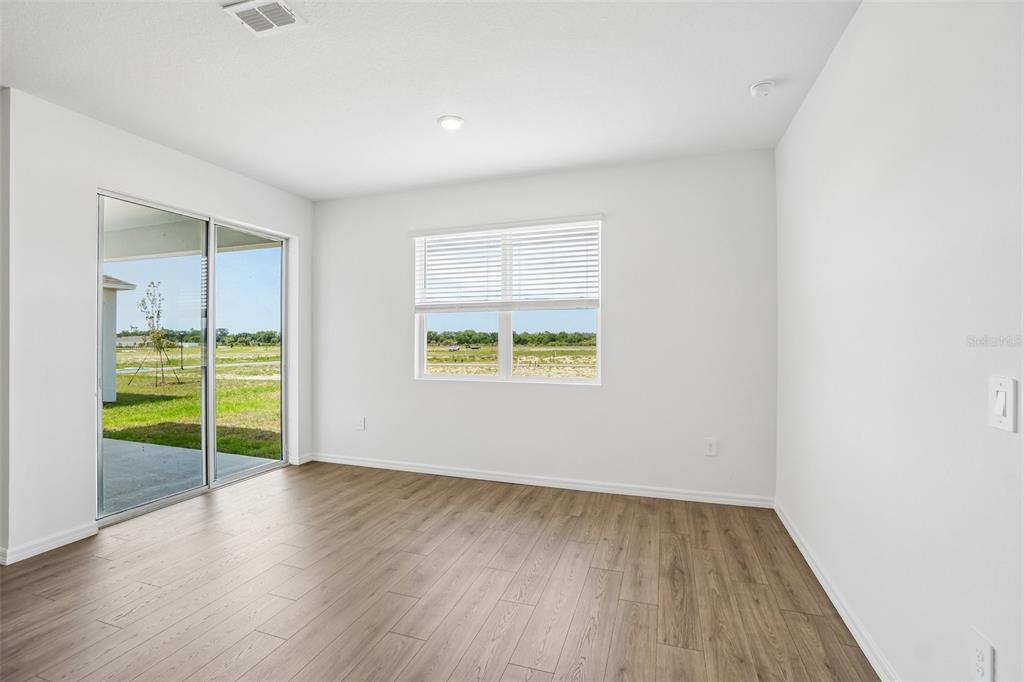 An empty room with light wood-look flooring, white walls, a sliding glass door, and windows — 1749 S HUMMINGBIRD ROAD, WINTER HAVEN, FL