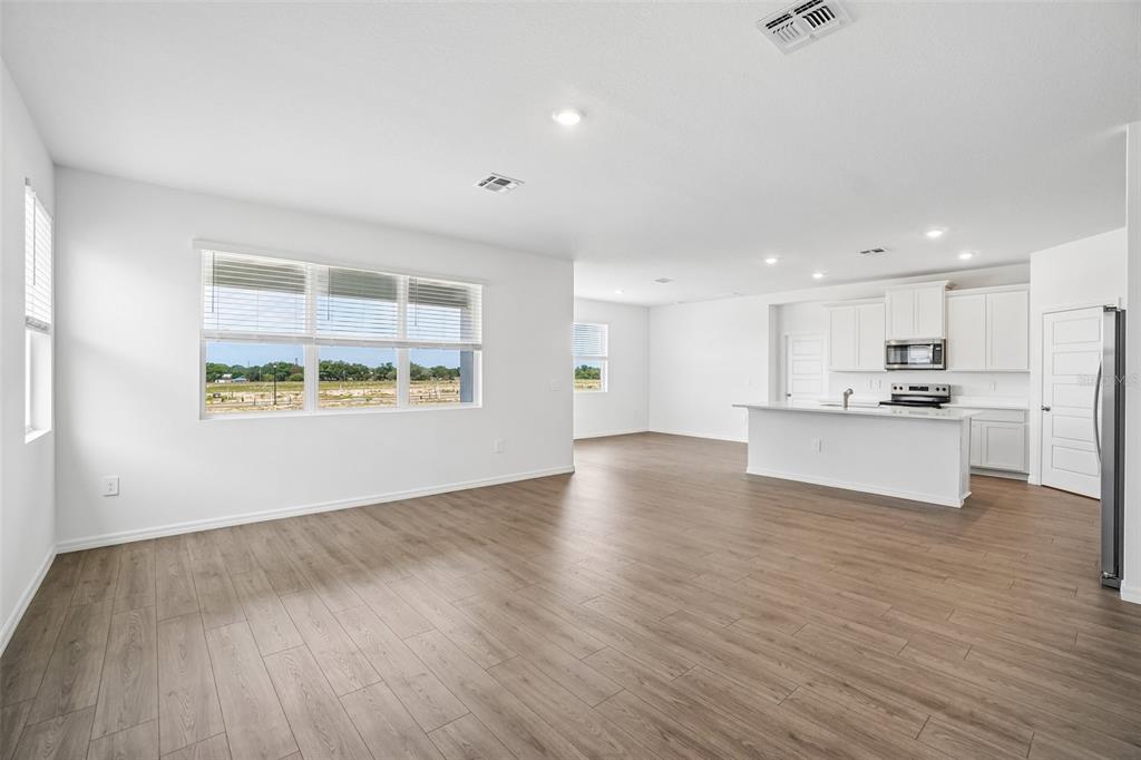 An open-concept living area with light wood-look flooring, white walls, and a modern kitchen — 1749 S HUMMINGBIRD ROAD, WINTER HAVEN, FL