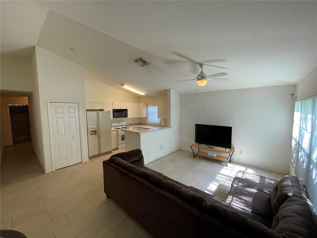 An open-concept living room features tile flooring, a brown sectional sofa, and an adjacent kitchen — 15120 DEER MEADOW DRIVE, LUTZ, FL