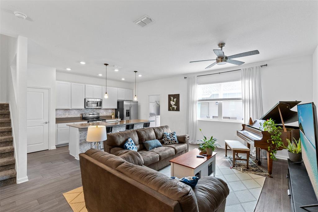 An open-concept living room and kitchen featuring a brown sectional, grand piano, and white cabinetry — 10607 WORDS DRIVE, WINTER GARDEN, FL