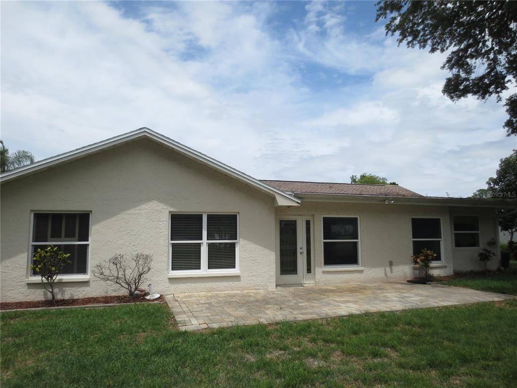 A beige stucco house features a paved patio and several windows under a cloudy sky — 3132 BRUNSWICK CIRCLE, PALM HARBOR, FL