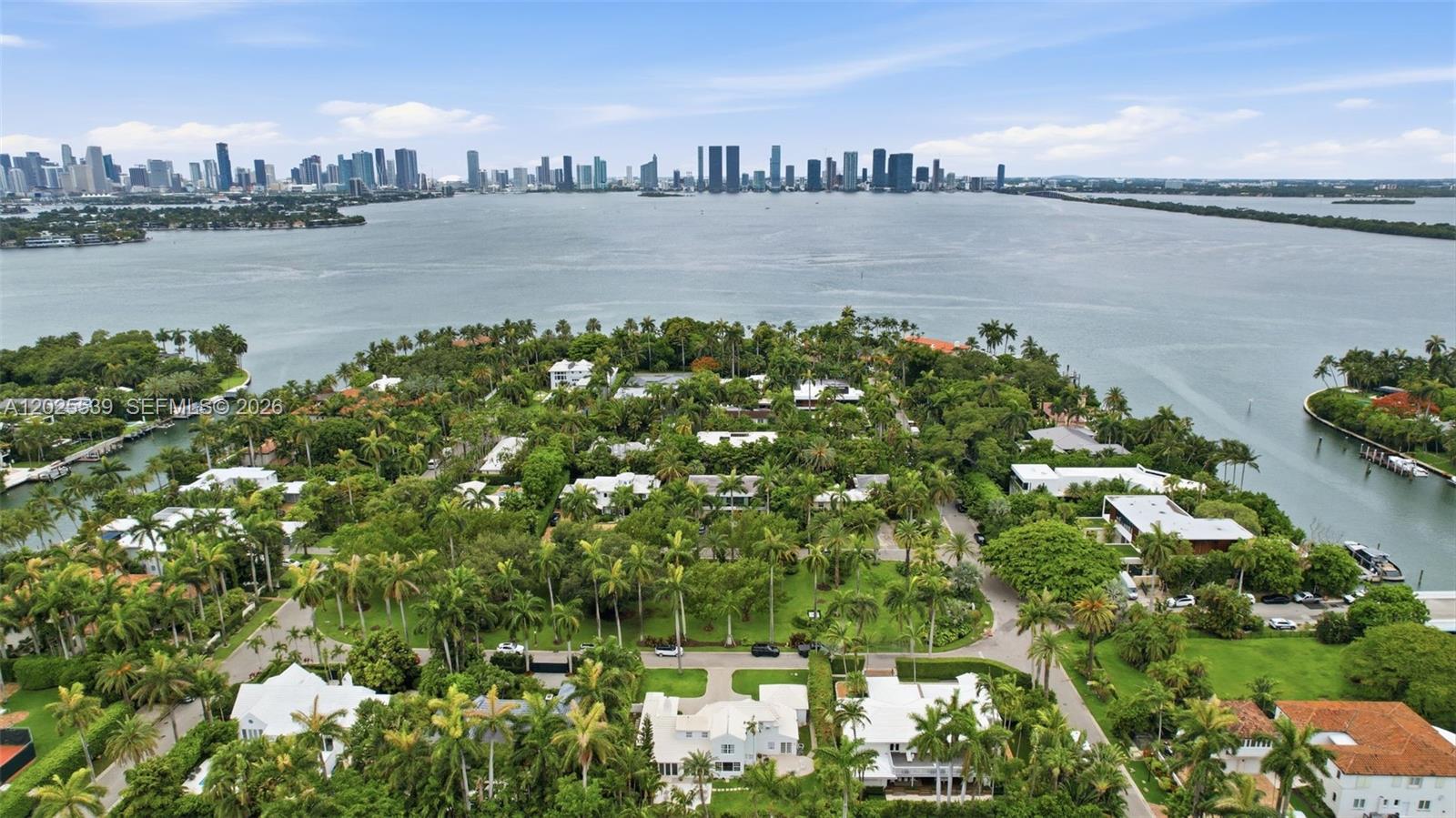 An aerial view shows a lush, tree-filled residential island surrounded by water with a city skyline — 2535 Sunset Dr, Miami Beach FL 33140, MIAMI BEACH, FL