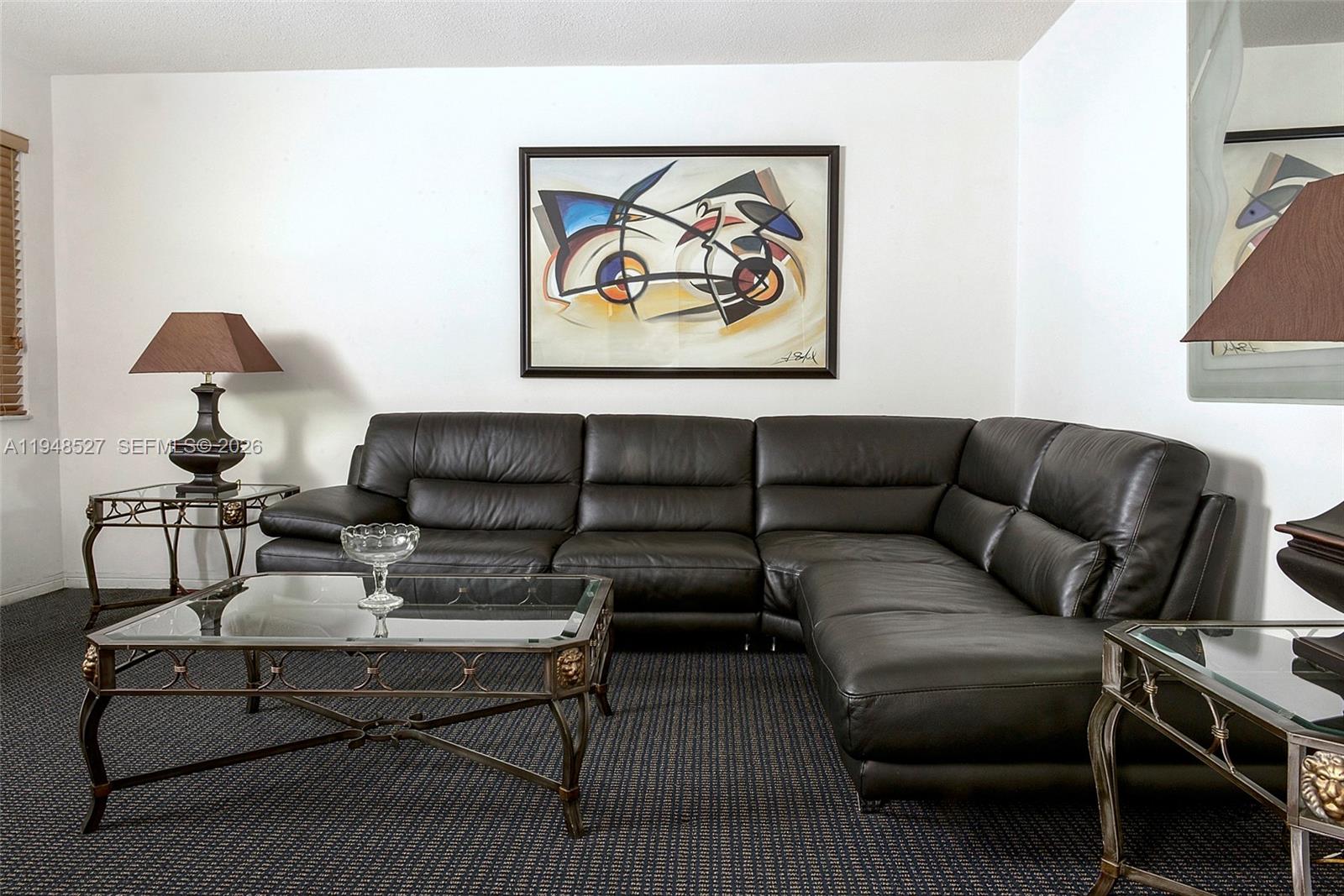 A living room features a dark leather sectional sofa, a glass coffee table, and abstract art — 1748 Rodman St # 117, Hollywood FL 33020, HOLLYWOOD, FL