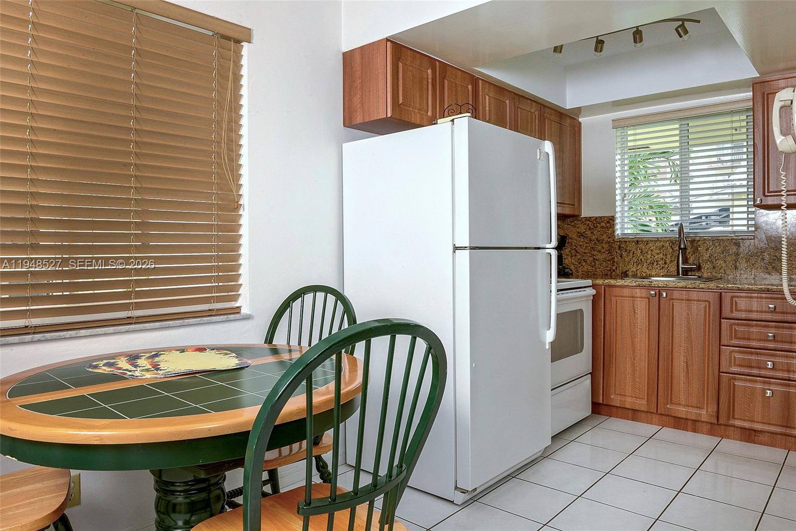 A kitchen features wood cabinets, a white refrigerator, a tile-topped dining table, and window blinds — 1748 Rodman St # 117, Hollywood FL 33020, HOLLYWOOD, FL