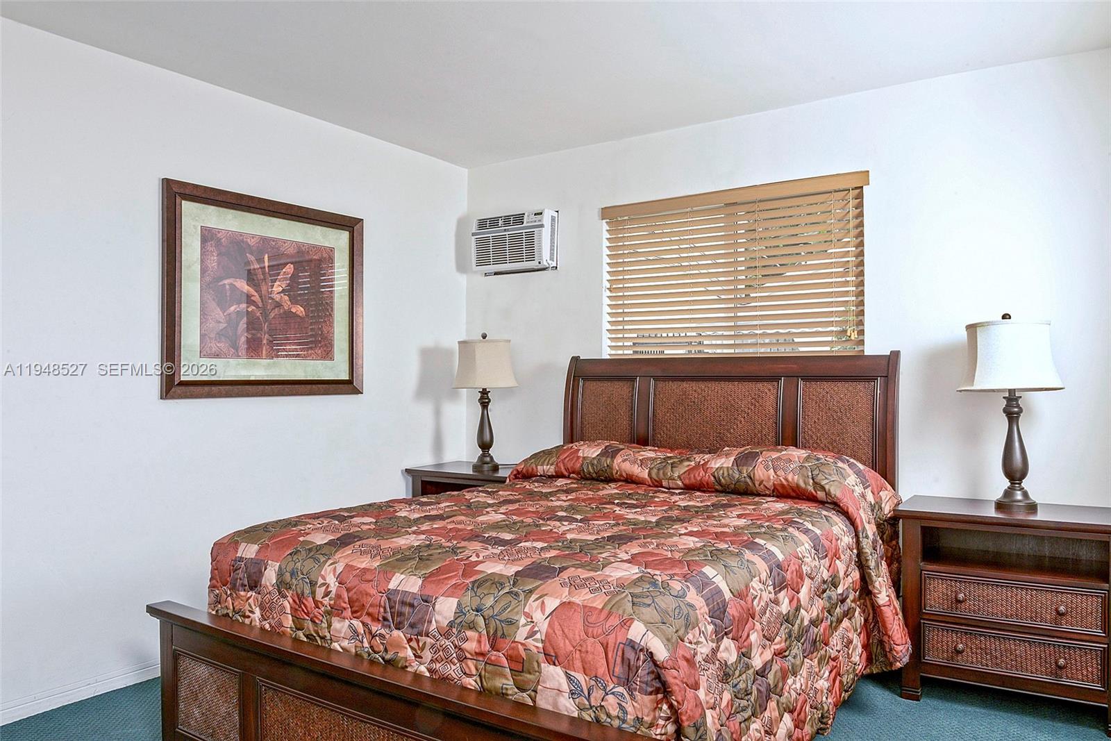 A bedroom features a wooden bed frame, patterned bedding, two nightstands, and a window — 1748 Rodman St # 117, Hollywood FL 33020, HOLLYWOOD, FL