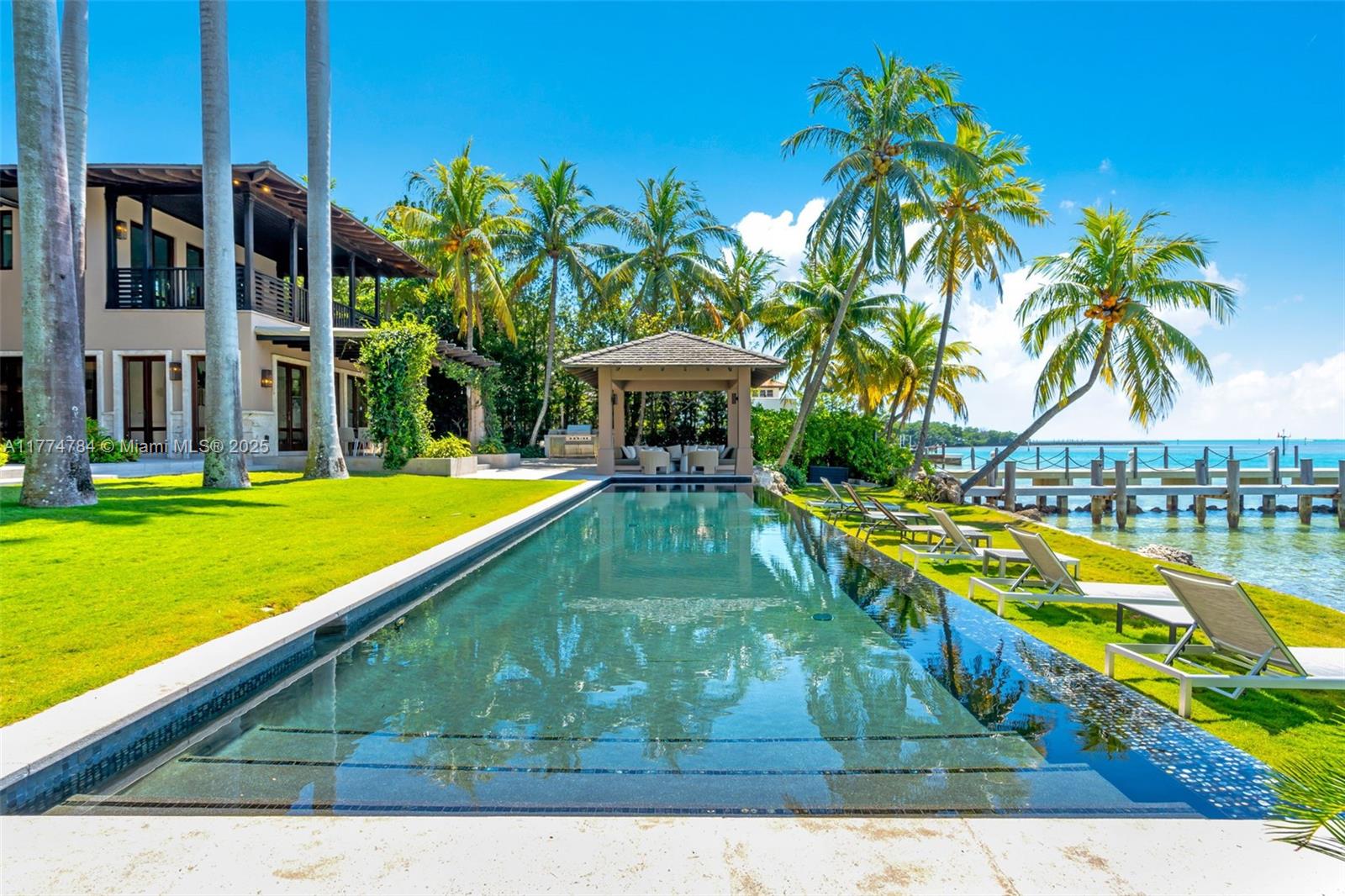 A long infinity pool sits on a grassy lawn beside a house and ocean dock — 9 Harbor Pt, Key Biscayne FL 33149, KEY BISCAYNE, FL