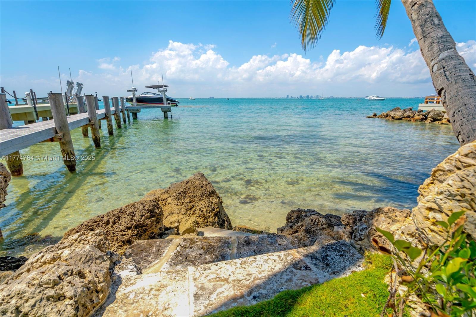 A wooden dock extends into clear water from a rocky shoreline with a palm tree — 9 Harbor Pt, Key Biscayne FL 33149, KEY BISCAYNE, FL