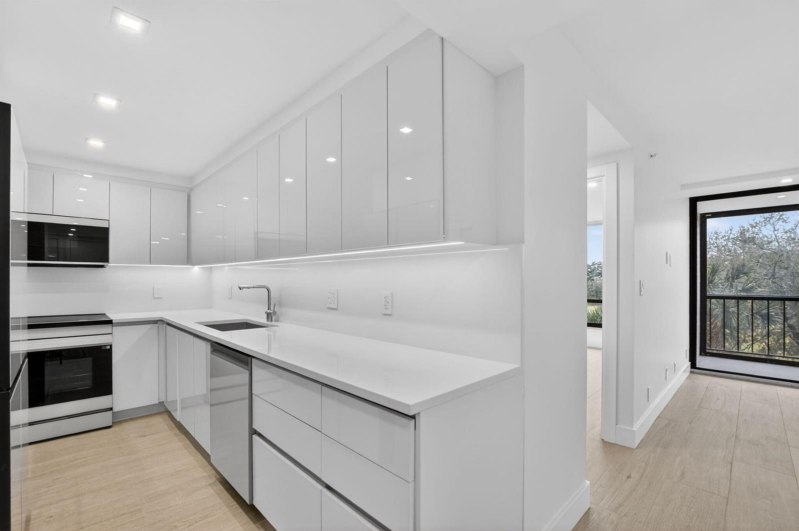 A modern white kitchen features glossy flat-panel cabinets, quartz countertops, and light wood-look flooring — 7835 Lakeside Boulevard # 946, Boca Raton FL 33434, BOCA RATON, FL