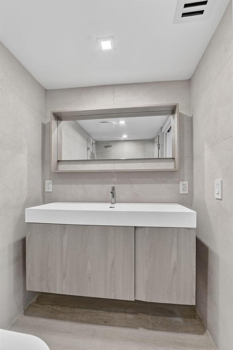 A modern bathroom features a floating wood vanity, a white sink, and a rectangular mirror — 7835 Lakeside Boulevard # 946, Boca Raton FL 33434, BOCA RATON, FL