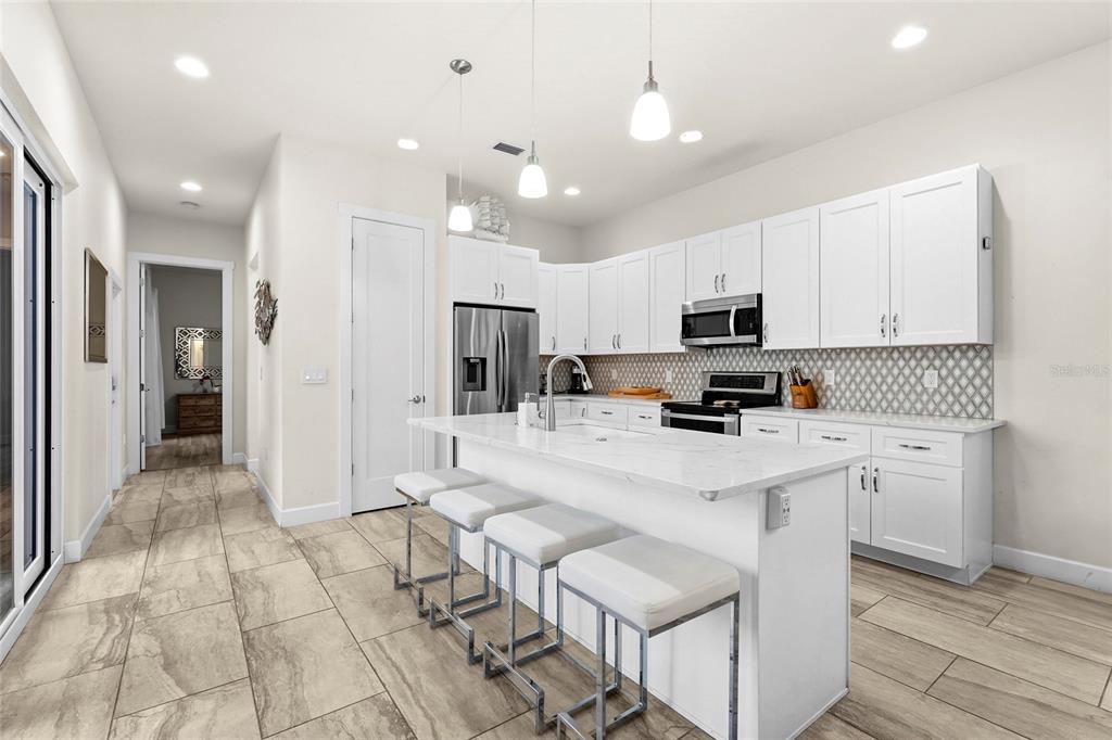 A modern kitchen features white cabinetry, a marble-topped island with bar seating, and tiled flooring — 1775 7TH STREET, SARASOTA, FL