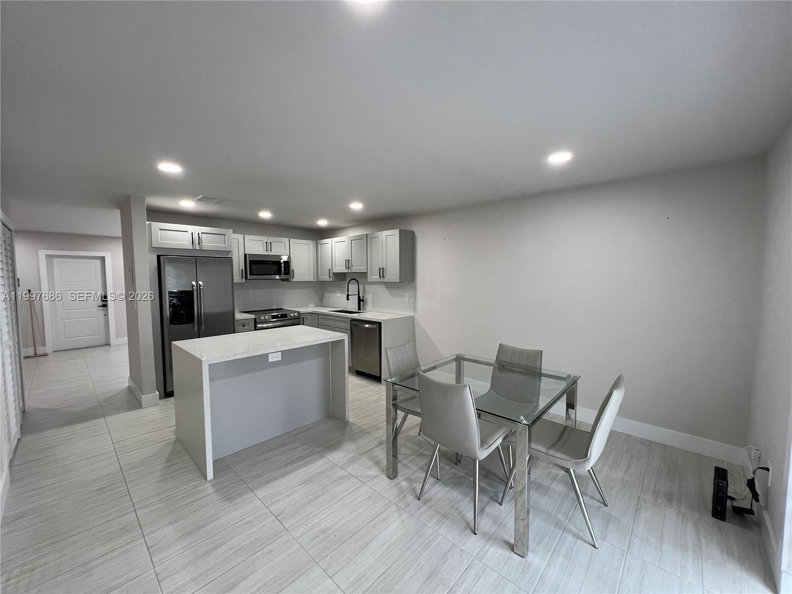 A modern kitchen features light gray cabinetry, stainless steel appliances, and a glass dining table — 3826 SW 107th Ave # 2, Miami FL 33165, MIAMI, FL