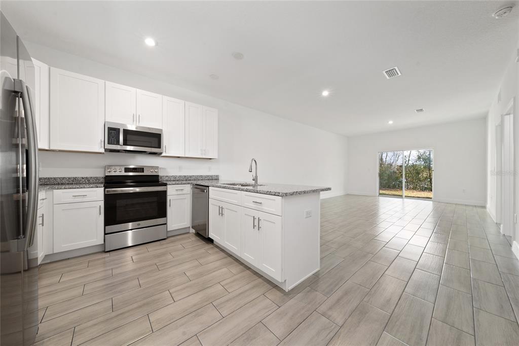 A kitchen with white cabinets, stainless steel appliances, and a granite island overlooks an open room — 462 LAKE SHORE PARKWAY, DAVENPORT, FL