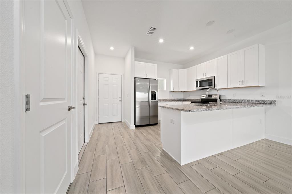 A kitchen with white cabinets, granite countertops, stainless steel appliances, and light wood-look tile flooring — 462 LAKE SHORE PARKWAY, DAVENPORT, FL