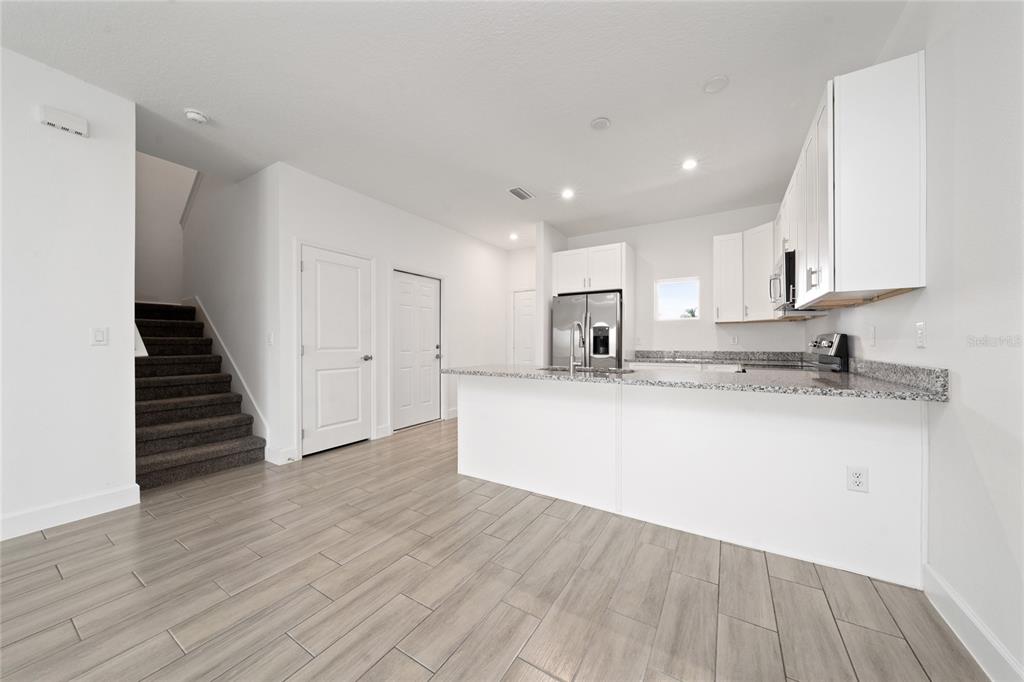 A kitchen with white cabinets, granite countertops, and a breakfast bar next to carpeted stairs — 462 LAKE SHORE PARKWAY, DAVENPORT, FL